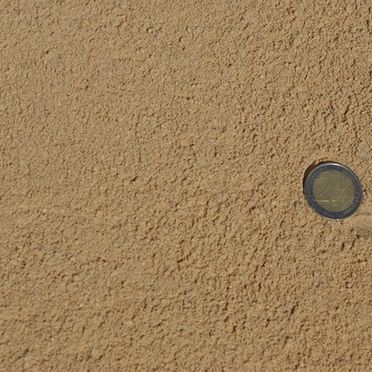 Un primer plano de una superficie arenosa con una moneda al lado.