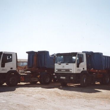 Tres camiones de volteo están estacionados uno al lado del otro en un camino de tierra.