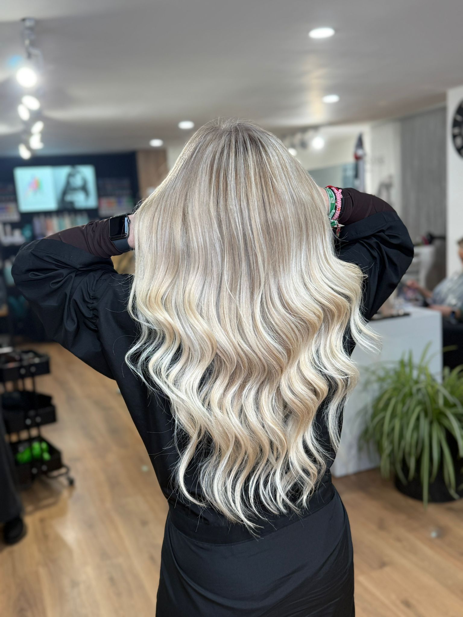 Mujer con cabello largo, ondulado y rubio en un salón; vistiendo un traje negro.