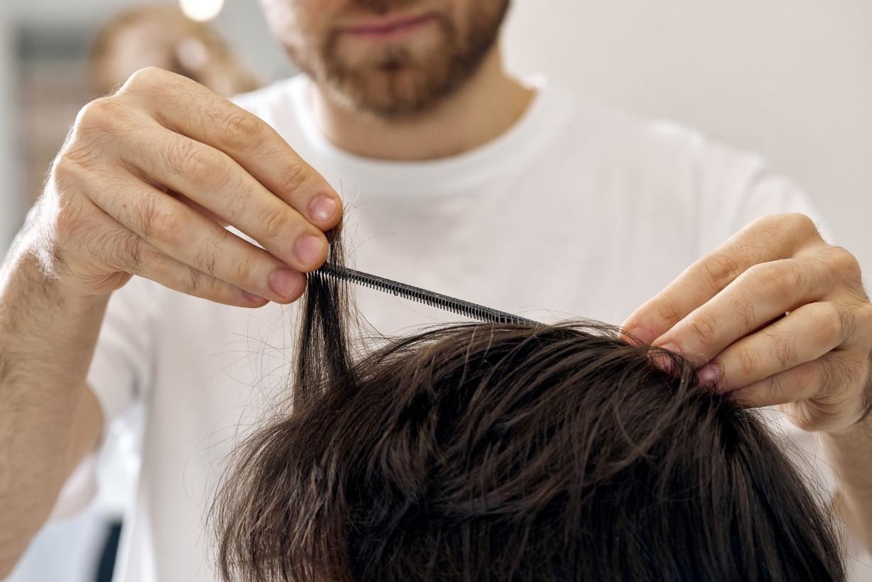 Barbero peinando el cabello oscuro de un cliente en un salón, preparándose para cortarlo.