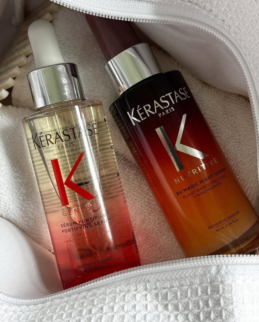 Dos frascos de suero capilar Kerastase sobre un paño blanco, uno transparente con rojo y otro ámbar.