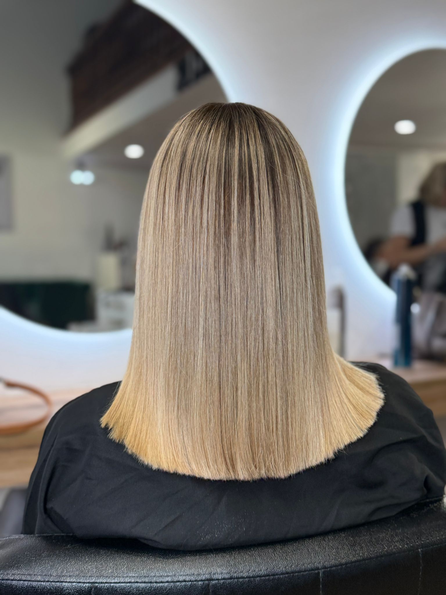 Cabello rubio en una silla de salón, peinado recto con un degradado de raíces más oscuras a puntas más claras.
