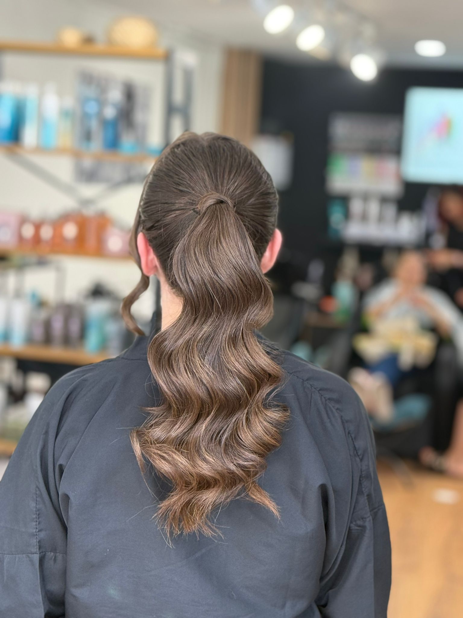Mujer con cabello castaño peinado en una cola baja y ondulada en una peluquería.