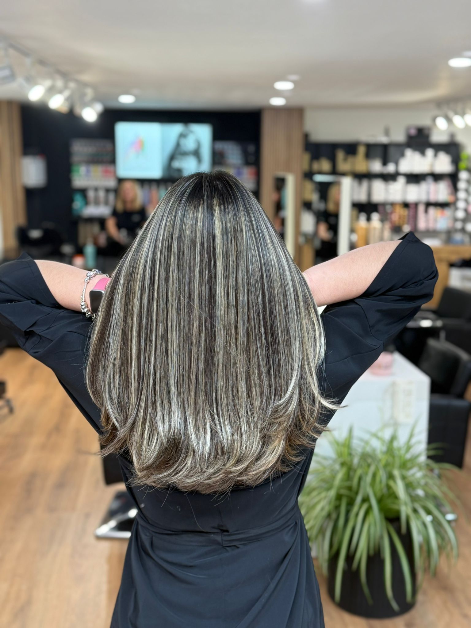 Mujer con mechas en una peluquería. Tiene los brazos levantados. Mechas rubias y castañas oscuras.