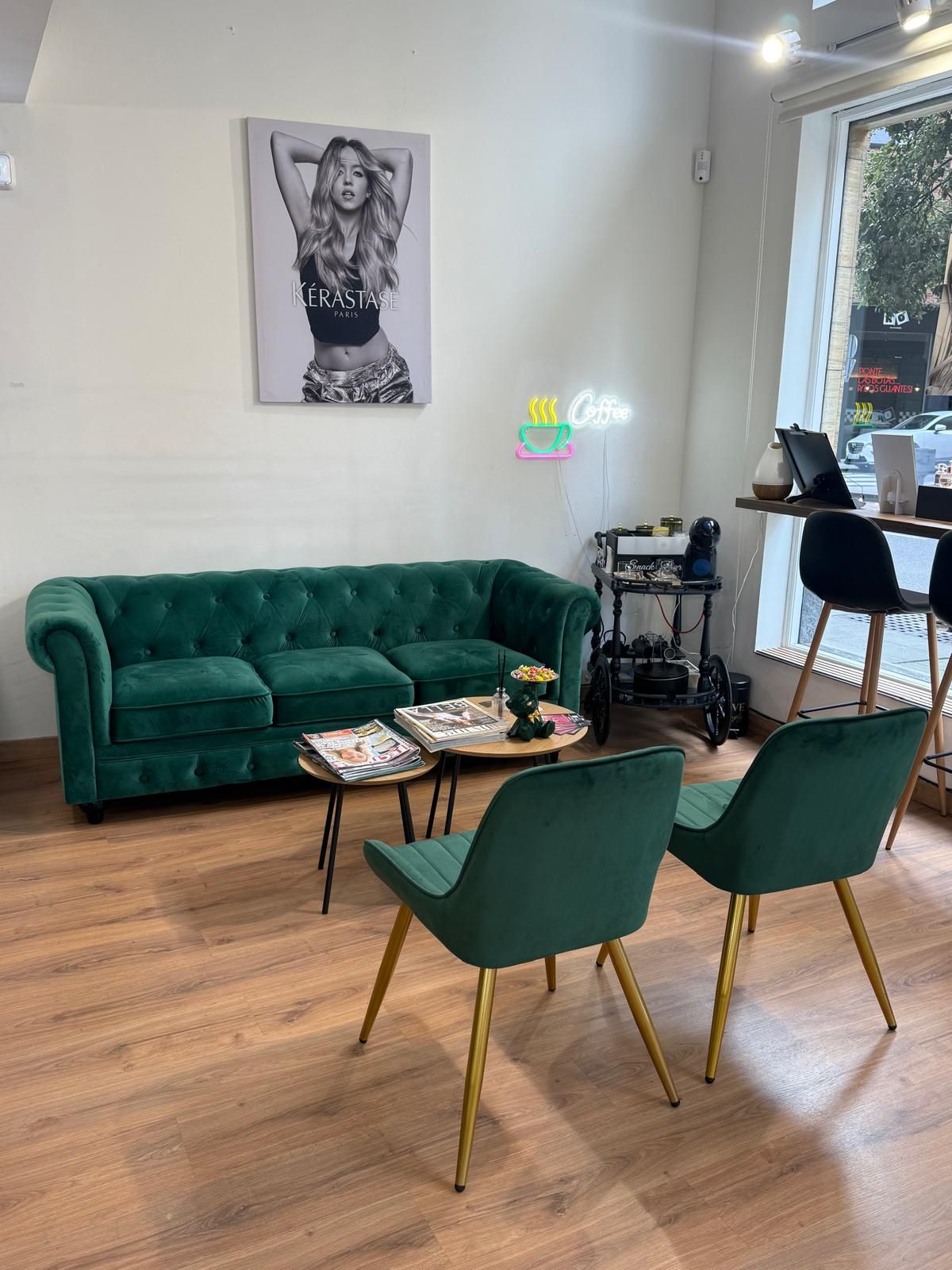 Zona de estar de terciopelo verde en un salón: sofá, dos sillas, mesas de café, obras de arte y un letrero de neón.