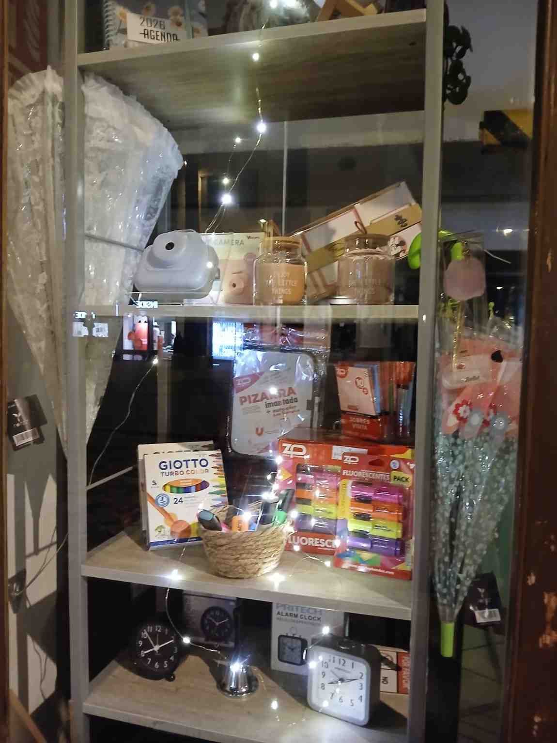 Estantería con diversos artículos: luces decorativas, cajas, reloj y flores.