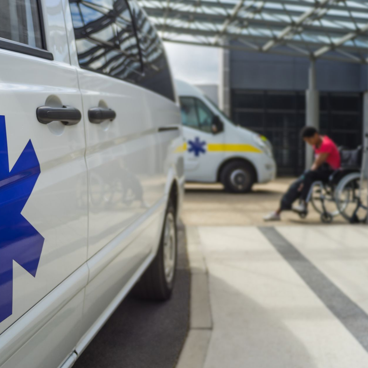 Une ambulance est stationnée près d'un bâtiment, avec une personne en fauteuil roulant à proximité.