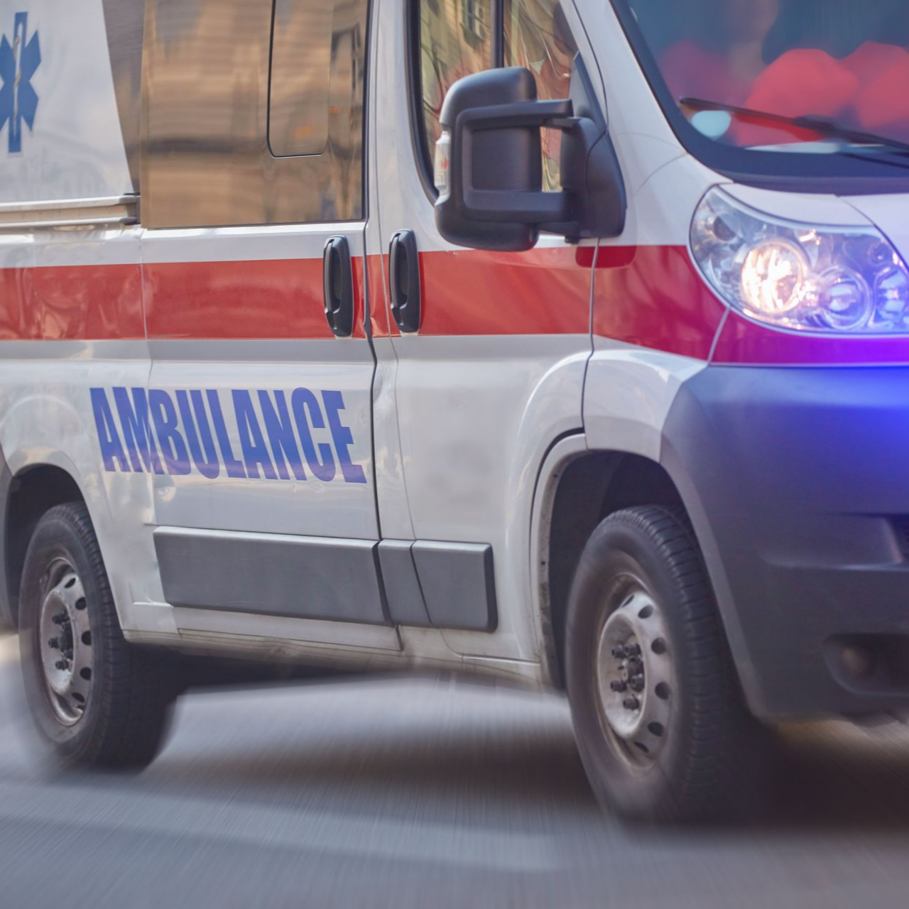 Une ambulance blanche avec une bande rouge et des gyrophares bleus circule dans la rue.