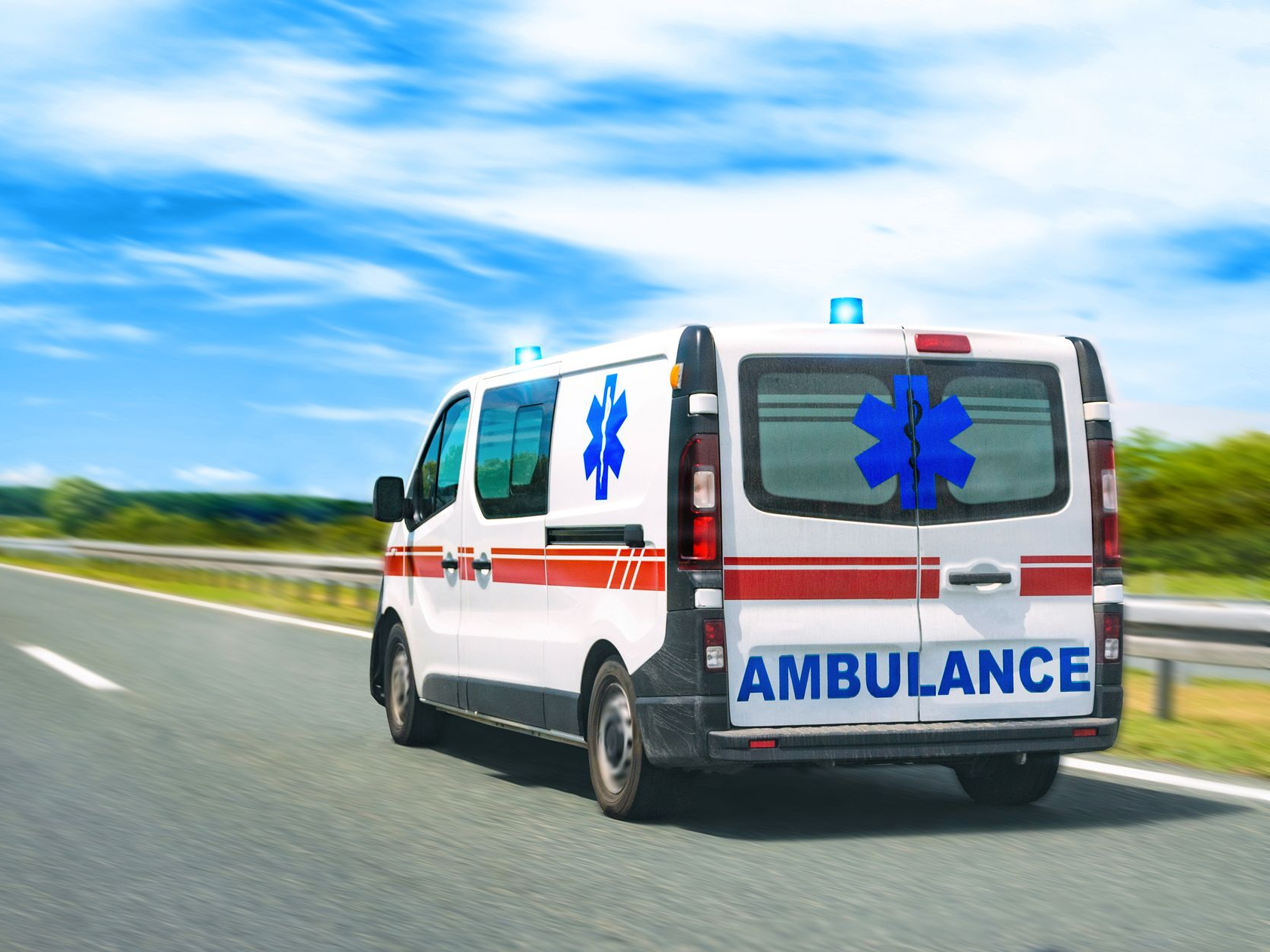Ambulance avec gyrophares allumés sur l'autoroute, ciel bleu.