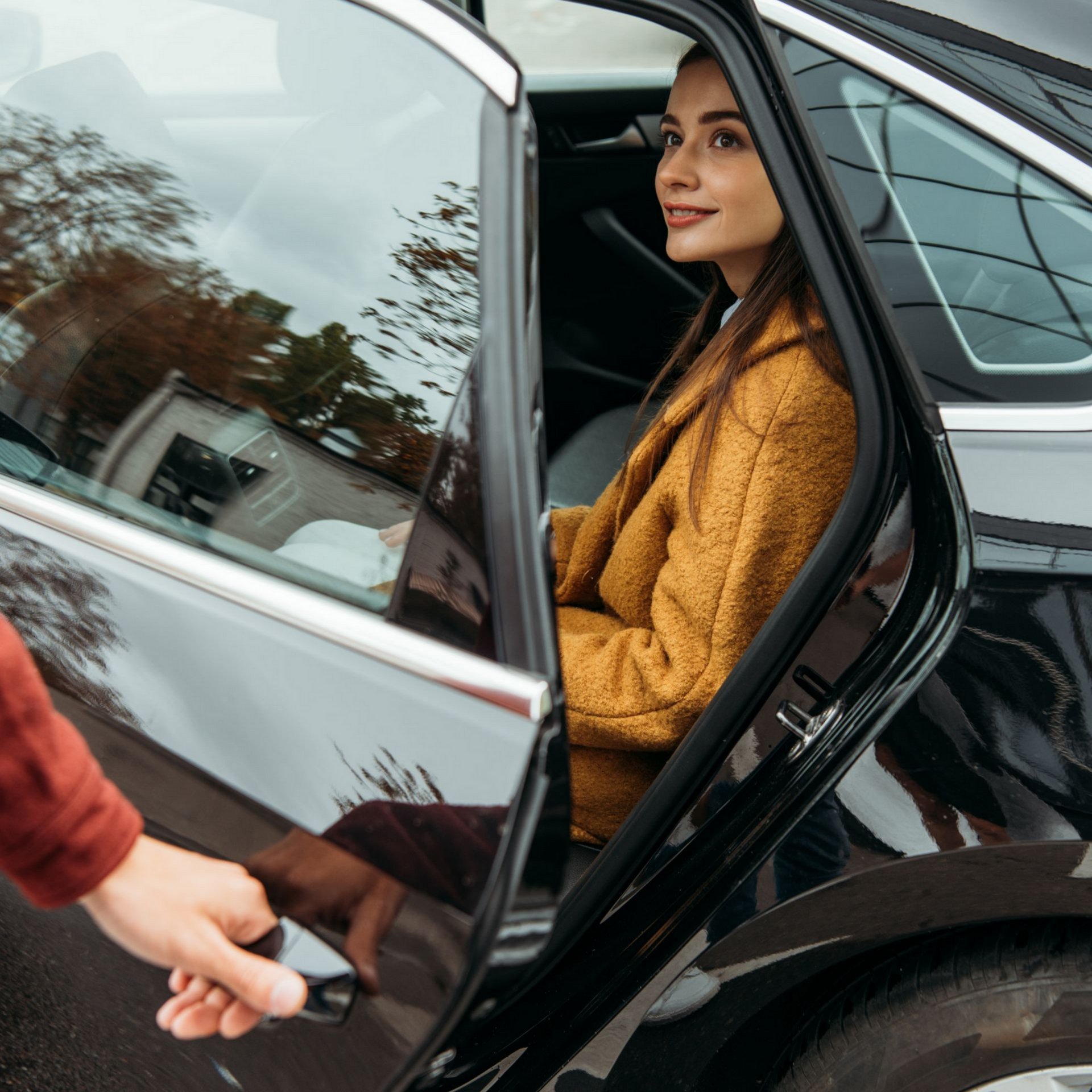 Une femme est assise dans une voiture, portière ouverte. Une main lui ouvre la portière.