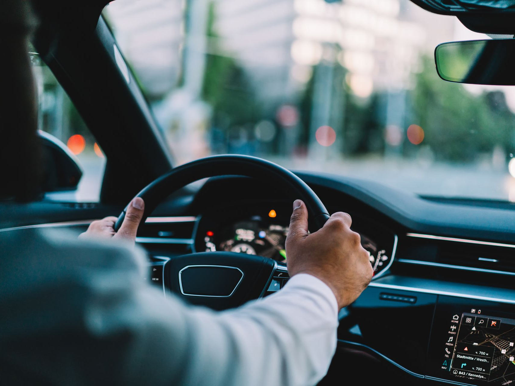 Des mains masculines tiennent le volant d'une voiture. Tableau de bord et ville floue en arrière-plan.