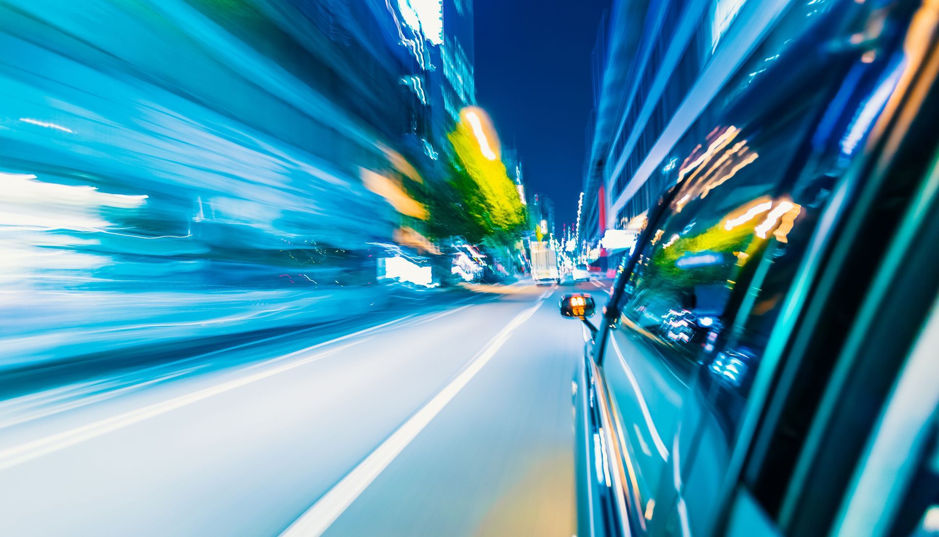 Voiture filant à toute allure dans une rue de la ville la nuit, lumières floues, traînées bleues et blanches éclatantes.