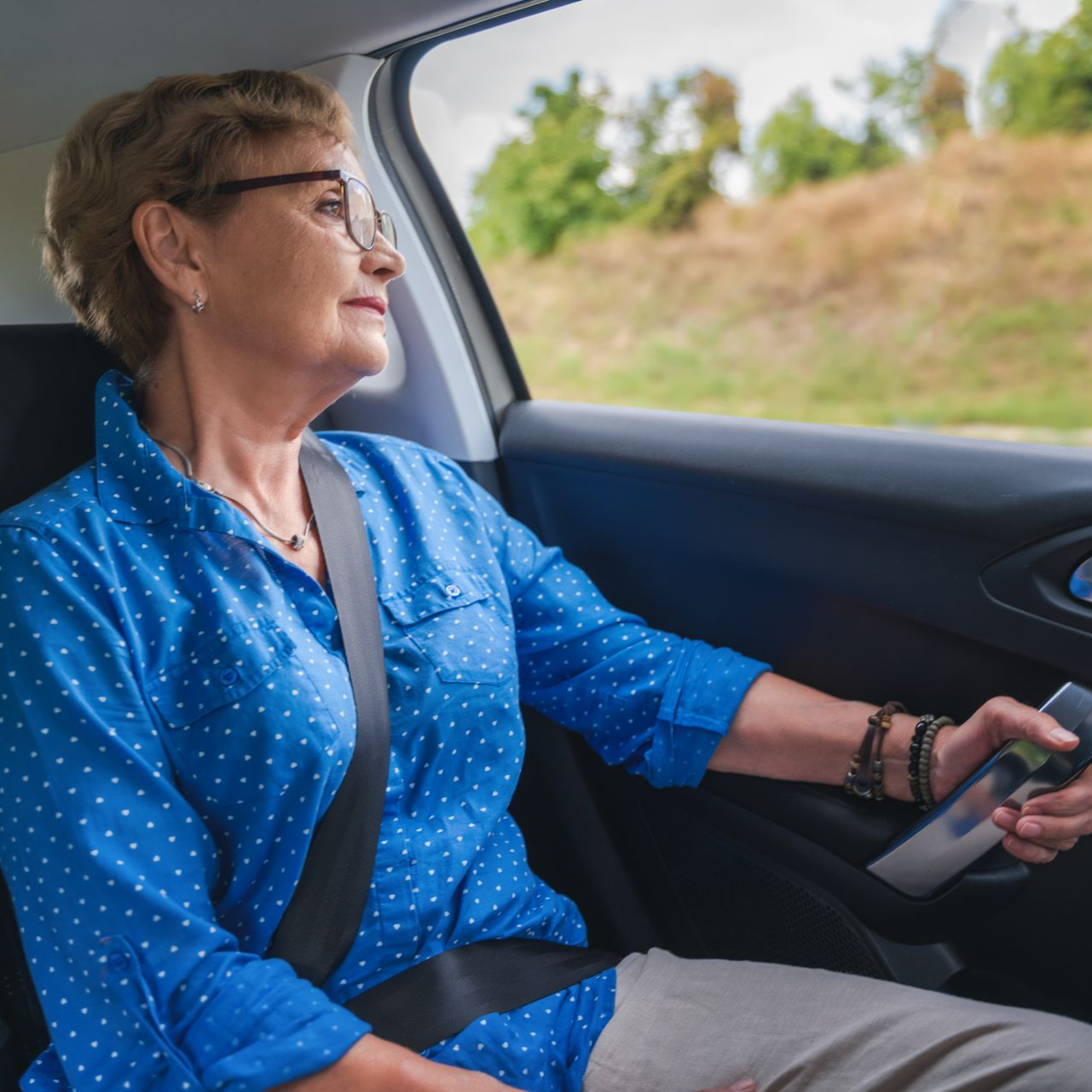Une femme en chemise bleue regarde par la fenêtre de la voiture, sa ceinture de sécurité est attachée.