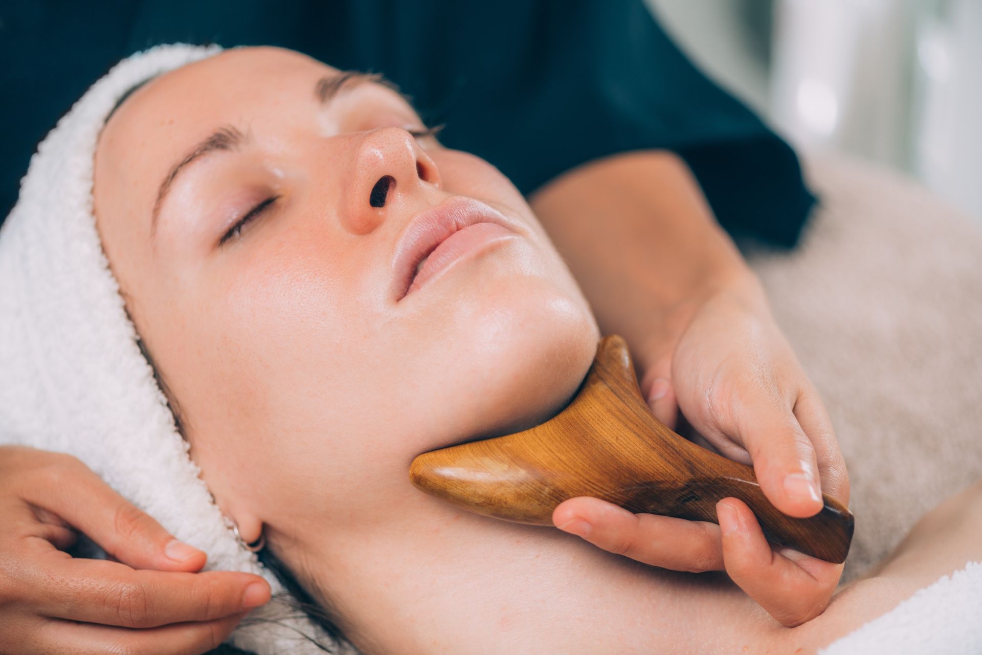 Mujer recibiendo un masaje facial con una herramienta de madera, con los ojos cerrados, en un entorno de spa.