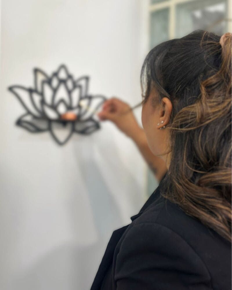 Mujer colocando una vela en una decoración de pared de flor de loto negra contra una pared blanca.