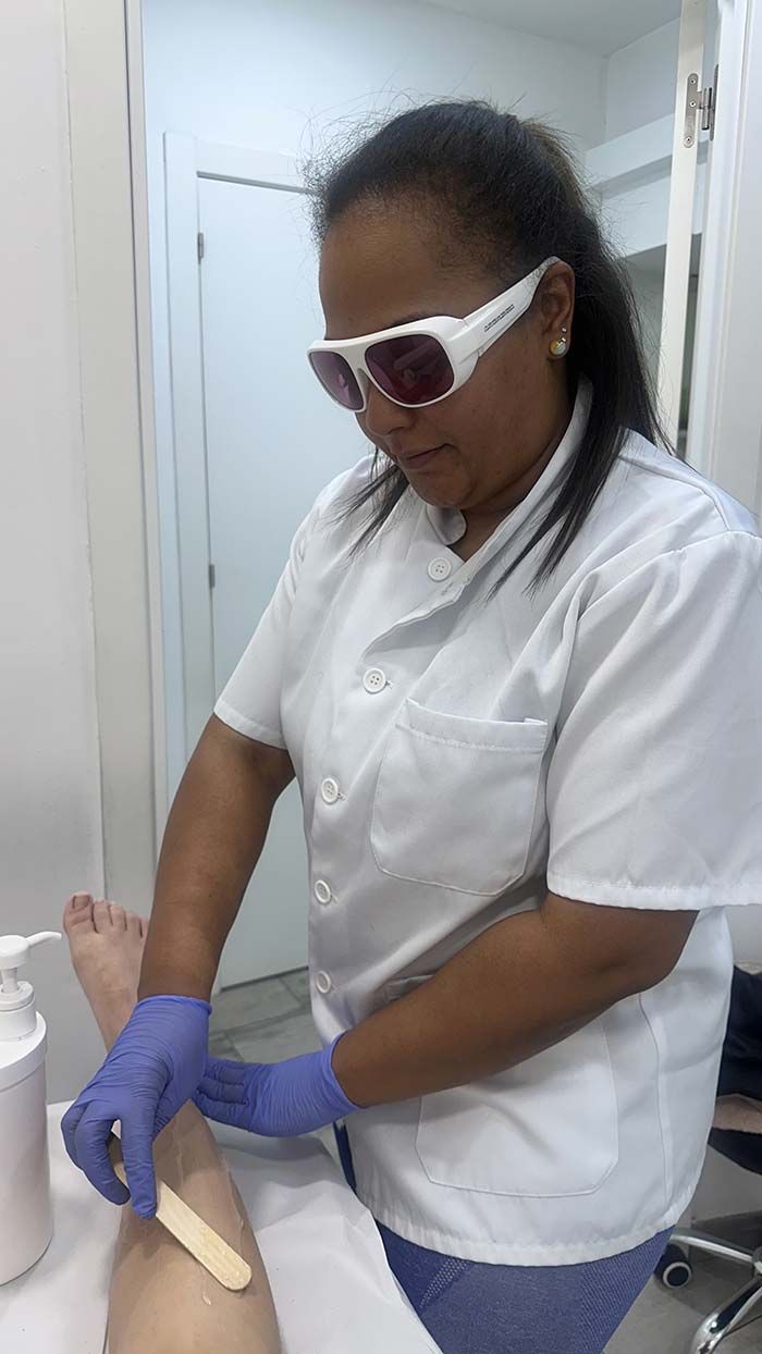 Mujer que usa gafas protectoras y se aplica cera en una pierna en un entorno médico.