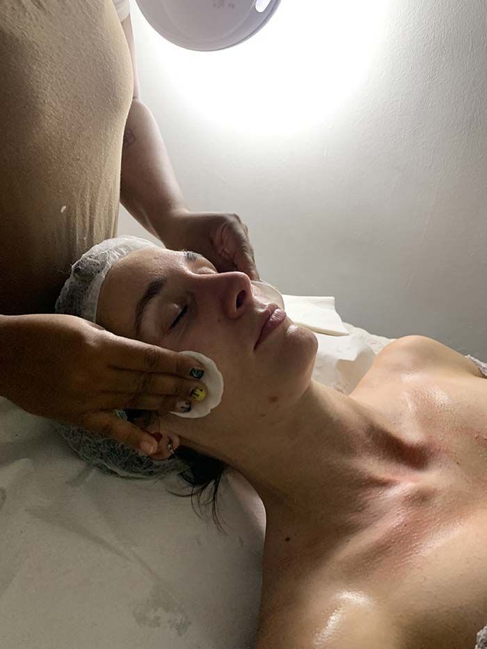 Persona recibiendo tratamiento facial en un spa. Una esteticista aplicando un producto con un disco de algodón. Luz blanca en el techo.