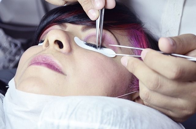 Una persona a la que un técnico le aplica extensiones de pestañas usando herramientas cerca del ojo.