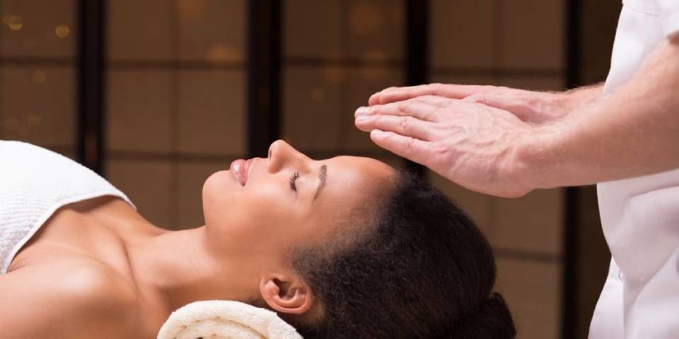 Ein Reiki-Praktizierender führt die Behandlung durch, indem er seine Hände über die Stirn einer Person hält.