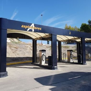 Estaciones de carga para vehículos eléctricos, cubiertas con marquesinas azules en una parada junto a la carretera, con dos cargadores a la vista.
