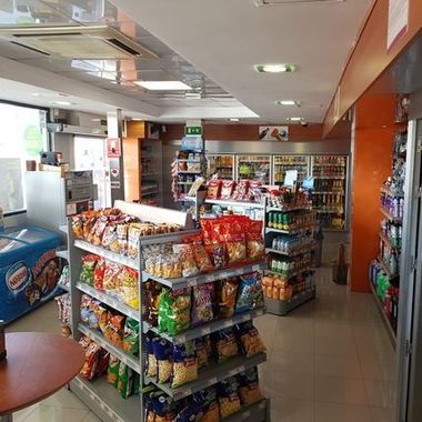 Pasillo de una tienda de conveniencia con estantes de snacks, bebidas y luces brillantes en el techo