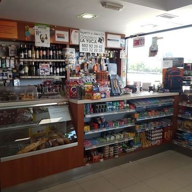 Mostrador de una tienda de conveniencia con aperitivos, bebidas y estanterías llenas de productos en un local luminoso