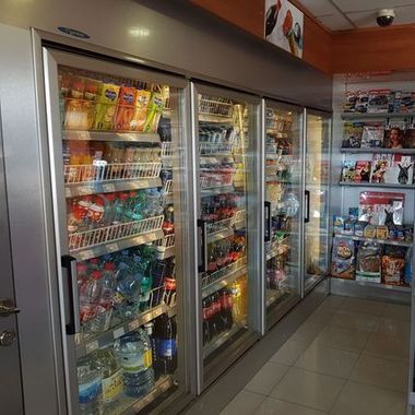 Pasillo de una tienda con refrigeradores de puertas de cristal llenos de bebidas y aperitivos.