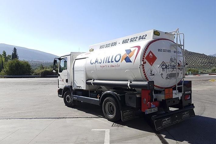 Camión cisterna de combustible blanco estacionado en un terreno, con montañas al fondo