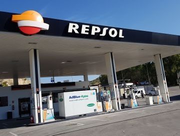 Marquesina de una gasolinera REPSOL, con surtidores de combustible y una furgoneta blanca bajo un cielo despejado