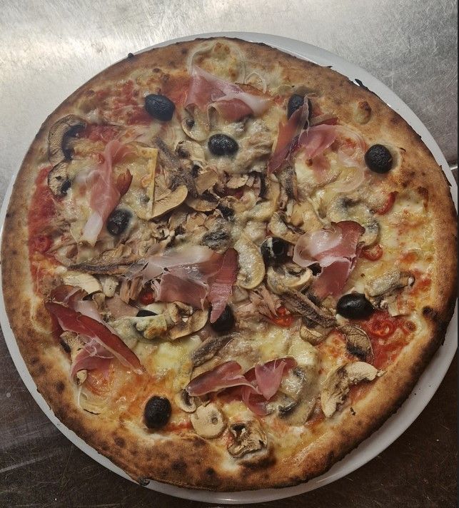 Mini pizza avec œuf, bacon, champignons et basilic sur une assiette blanche.