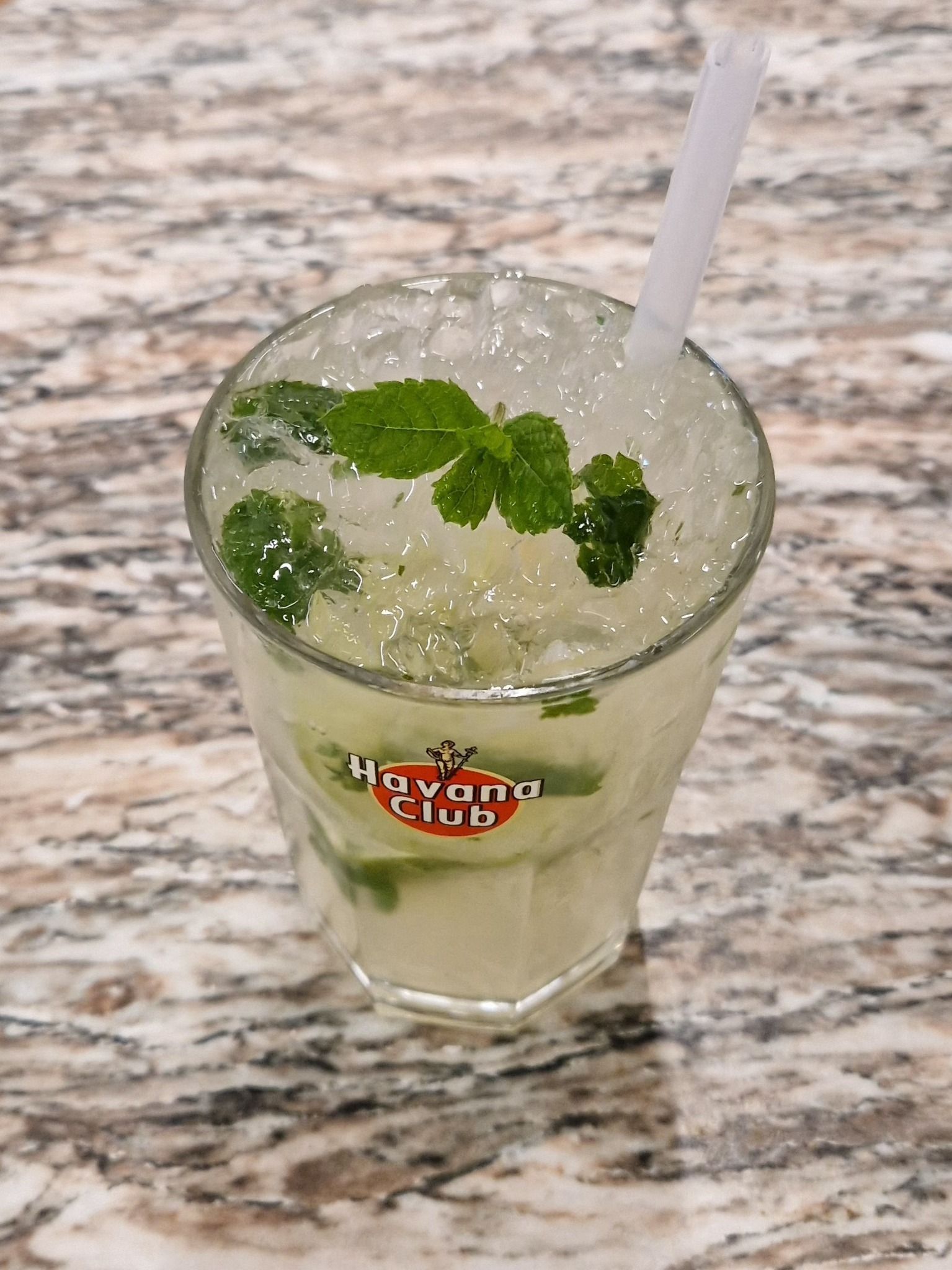 Cocktail Mojito dans un grand verre, garni de menthe, sur un comptoir en marbre.