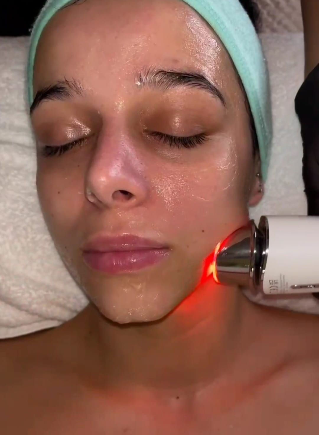 Una mujer está recibiendo un tratamiento facial con una luz roja en su cara.