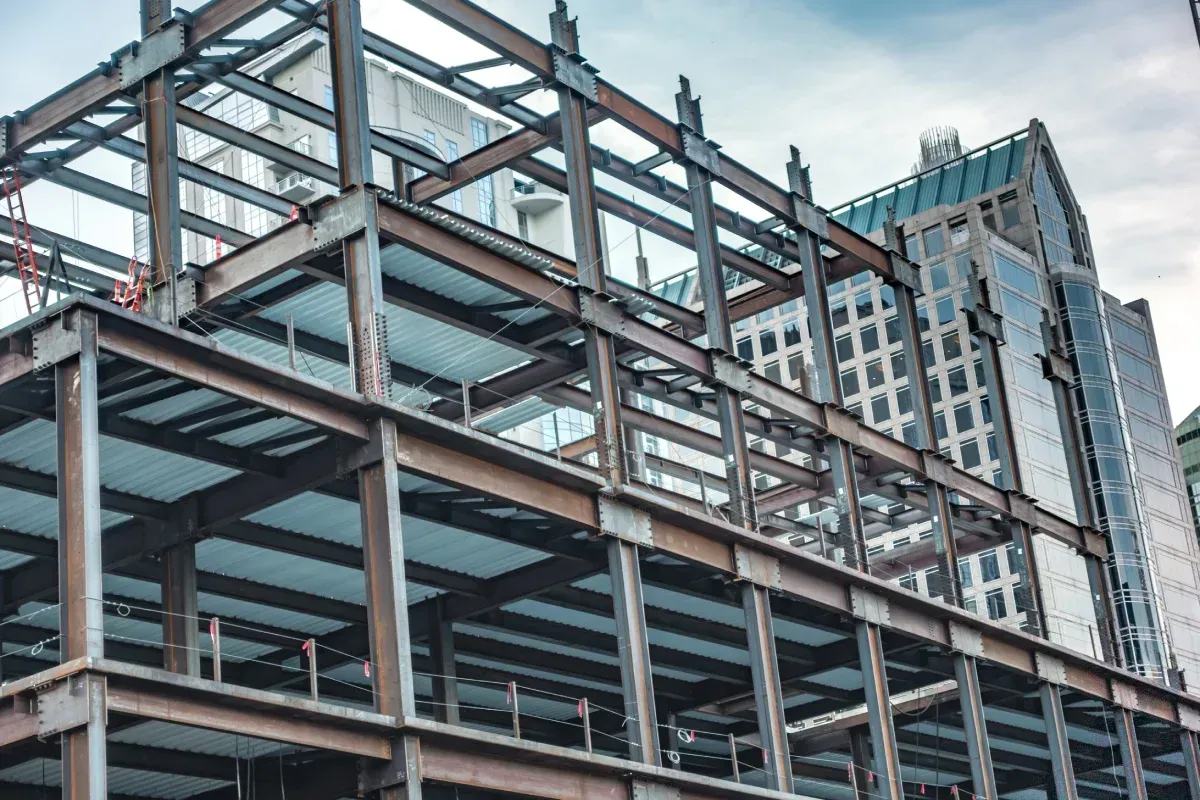 Estructura de acero de un edificio en construcción, con otros edificios al fondo.