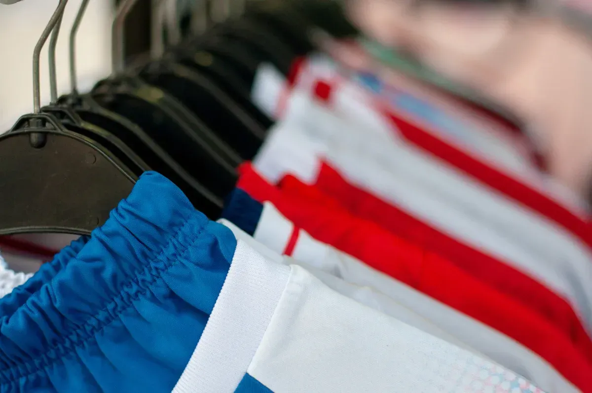 Una hilera de pantalones cortos deportivos azules, blancos y rojos cuelgan de perchas negras.