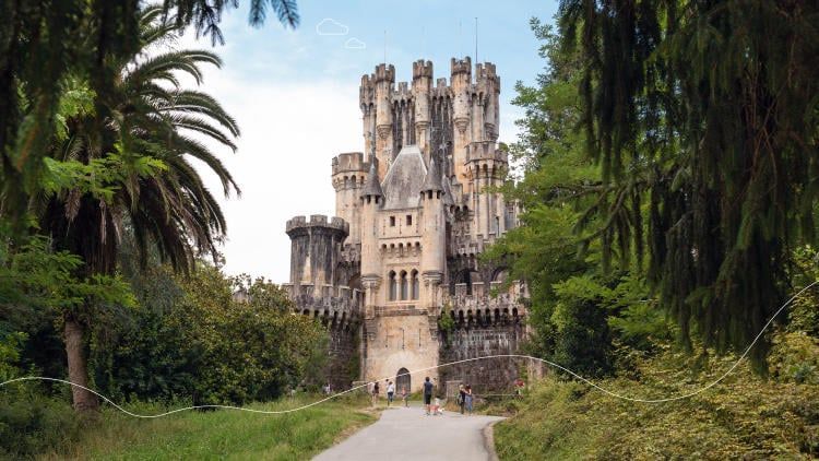 Castillo medieval enmarcado por exuberantes árboles verdes, el camino conduce a la entrada en un día soleado.