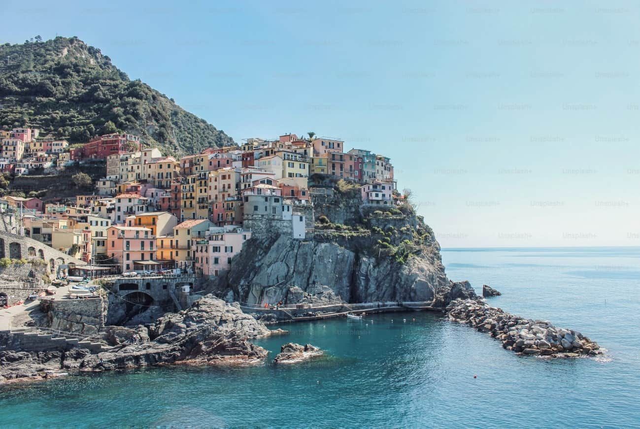 Pueblo costero de edificios coloridos encaramado en un acantilado, con vistas al mar azul. Día soleado.