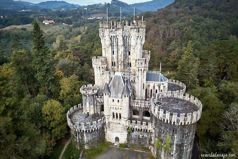 Castillo de piedra con múltiples torres y almenas, rodeado de árboles.