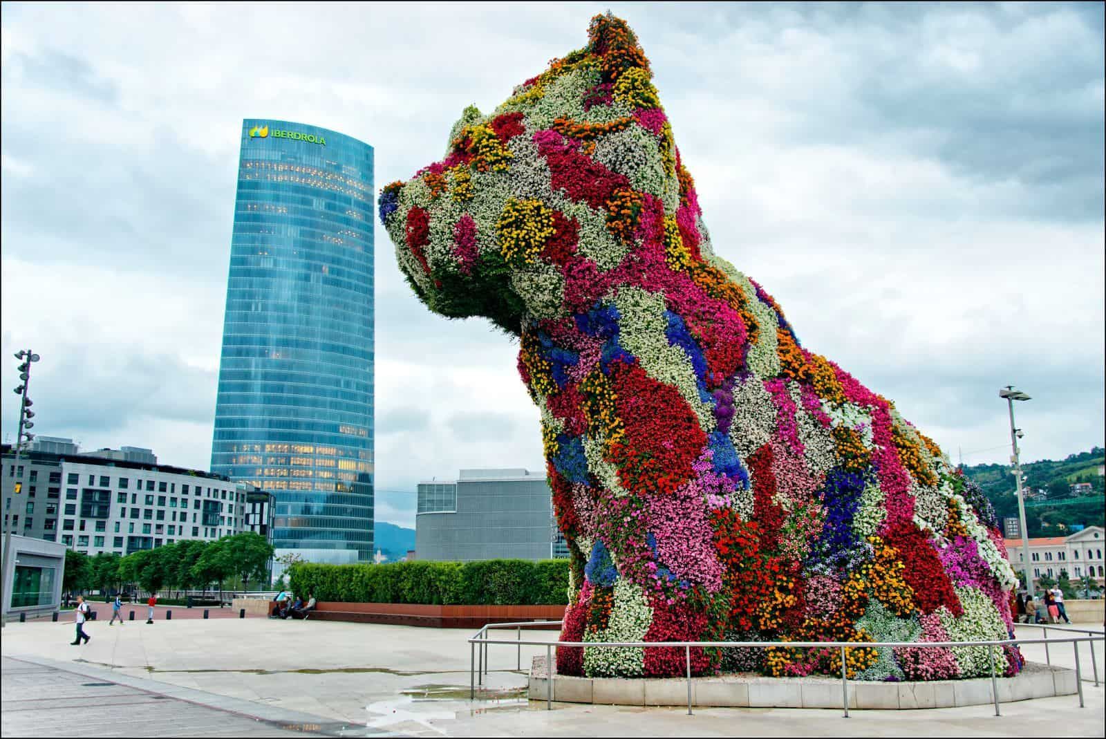 Viñedo al amanecer, hileras de vides verdes, camino de tierra, sol brillante en un cielo azul y nublado.