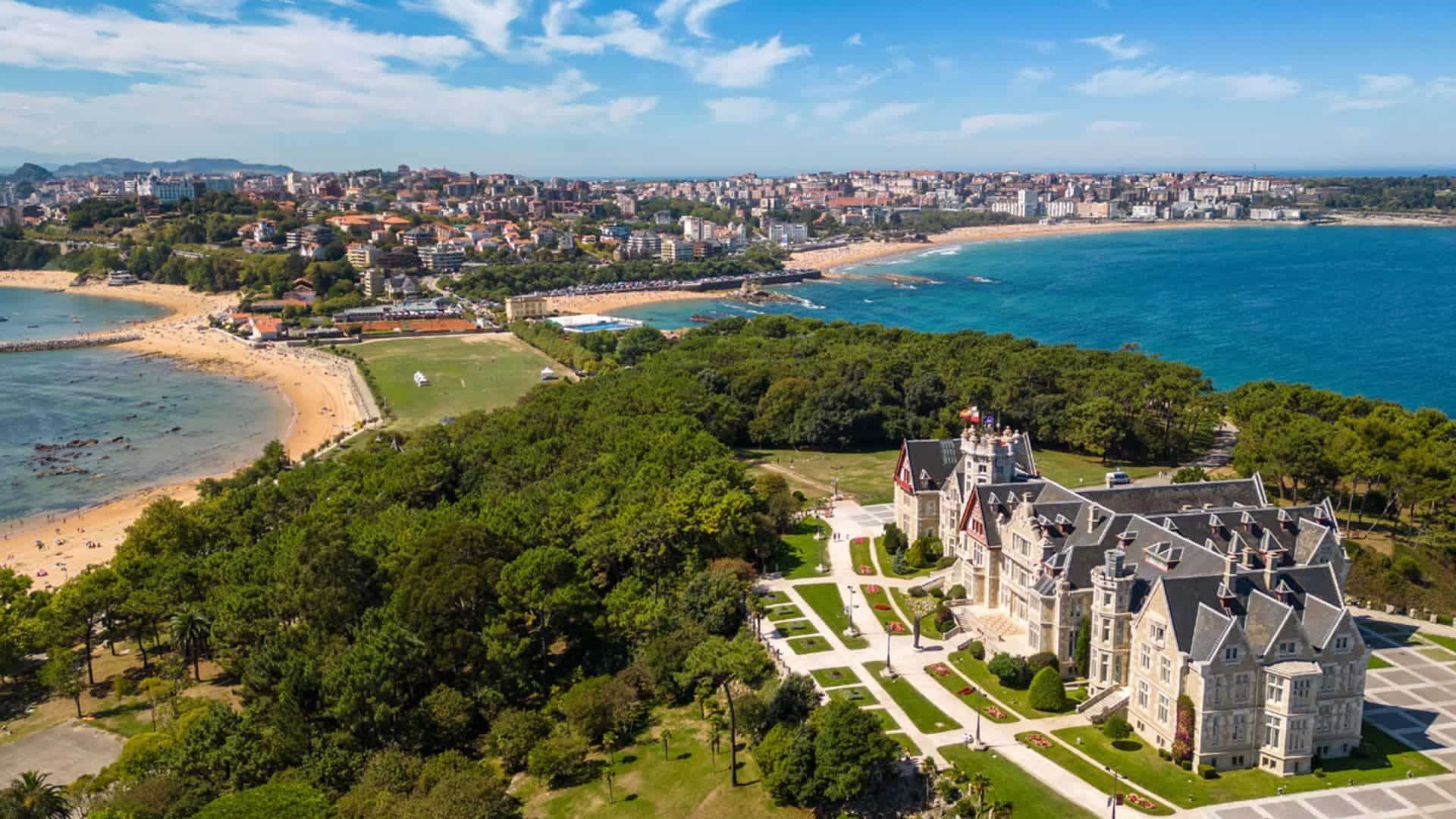 Vista aérea costera de una ciudad con un gran castillo, playas y el mar. Cielo azul y soleado.