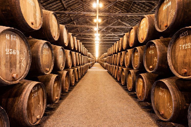 Filas de barriles de madera en una bodega poco iluminada, posiblemente para añejar vino.