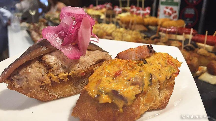 Dos tapas en plato blanco: una cubierta con carne y cebolla encurtida, y la otra con una salsa amarilla.