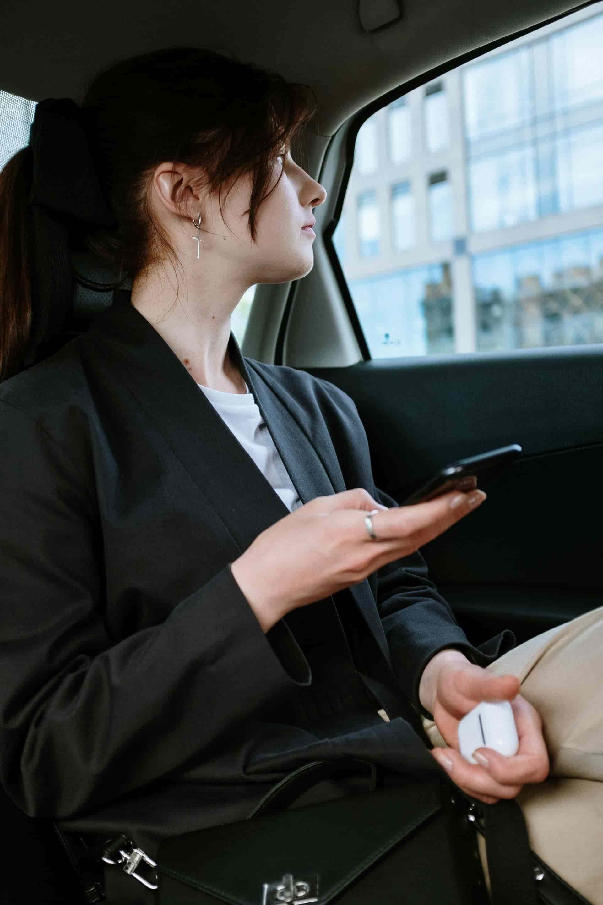 Mujer en un coche sosteniendo un teléfono y auriculares, mirando por la ventana.