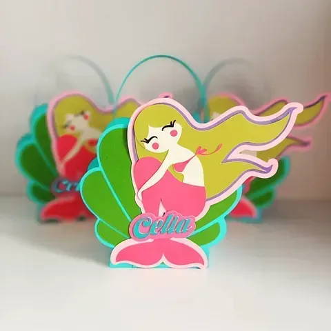Adorno de fiesta colorido con forma de hada amarilla sobre una base rosa y verde con el nombre 