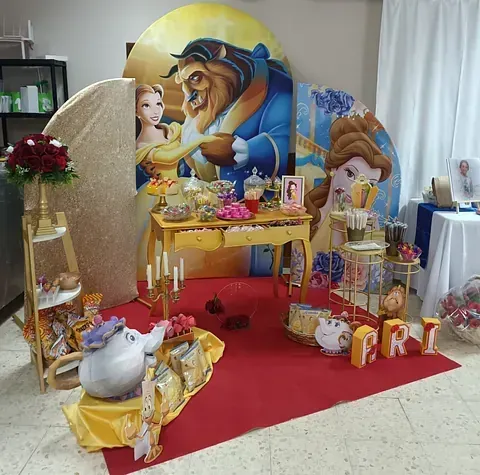 Altar decorado con temática de La Bella y la Bestia con velas, flores, regalos y una alfombra roja.