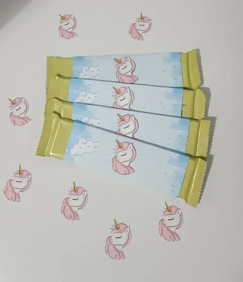 Cuatro barras de chocolate con forma de unicornio de color azul claro y amarillo sobre una superficie blanca con estampados de unicornios rosas.