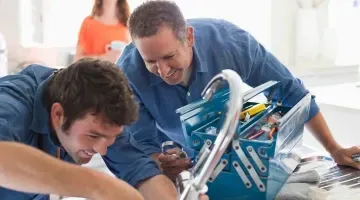 Dos hombres están trabajando en un fregadero con una caja de herramientas.