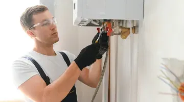 Un hombre está arreglando un calentador de agua en la pared.