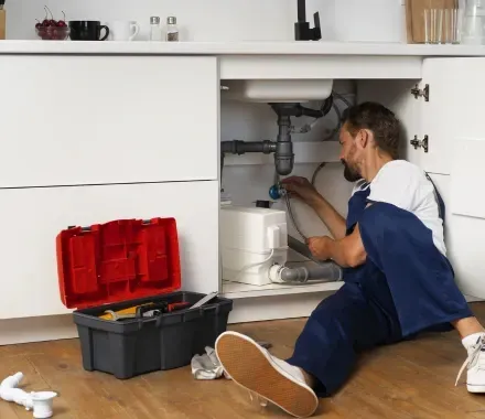 Un fontanero está arrodillado debajo de un fregadero de cocina.