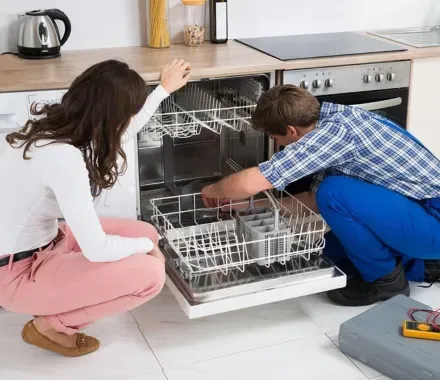Un hombre y una mujer están trabajando en un lavavajillas en una cocina.