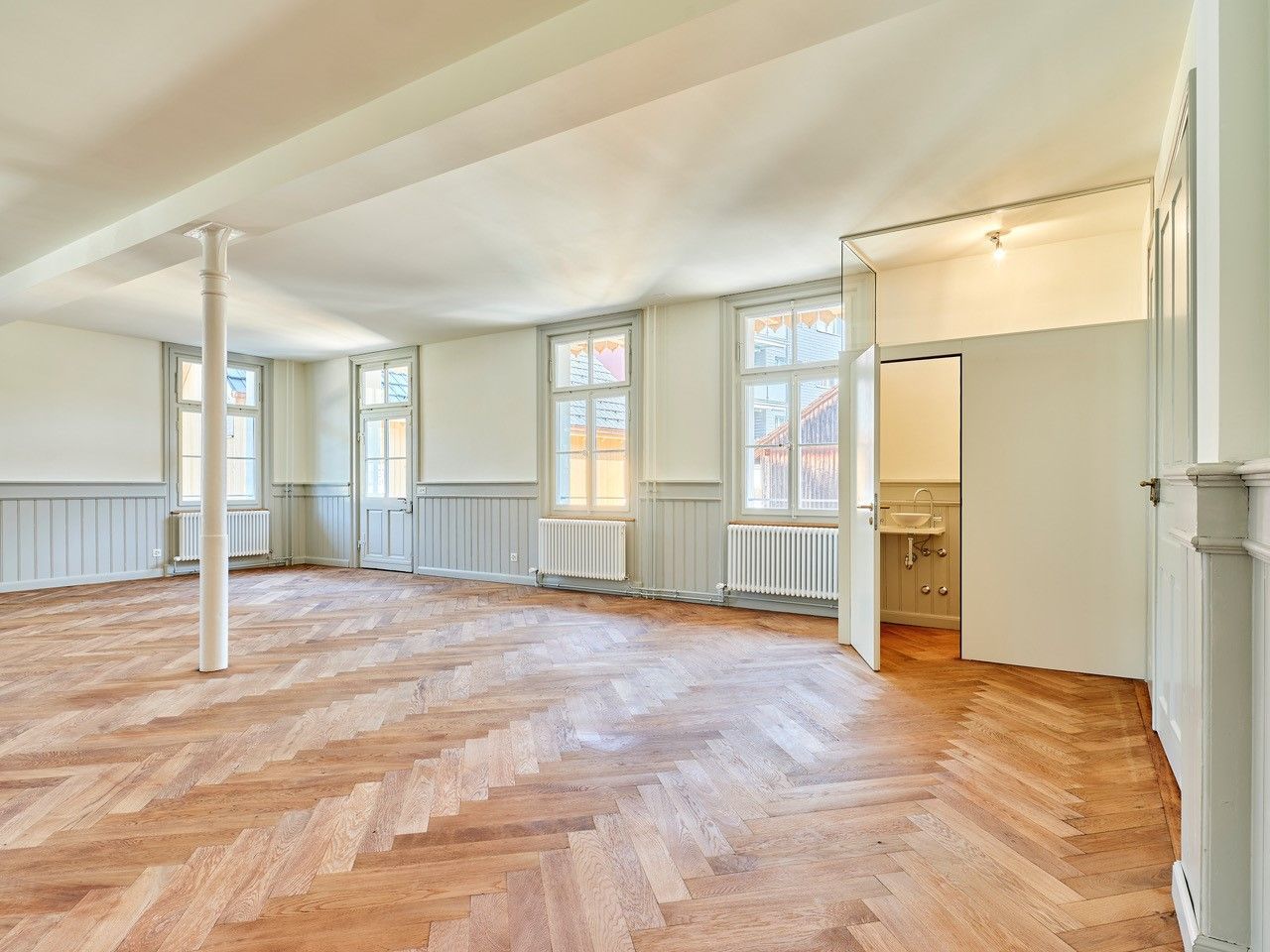 Ein großer, leerer Raum mit Holzboden und weißen Wänden.